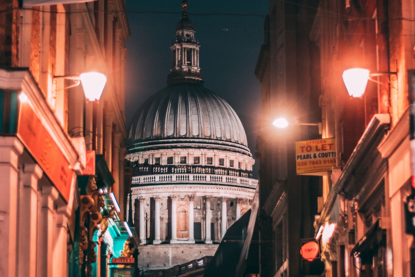 St Paul's Cathedral framed by lamplit buildings on a London street at night.