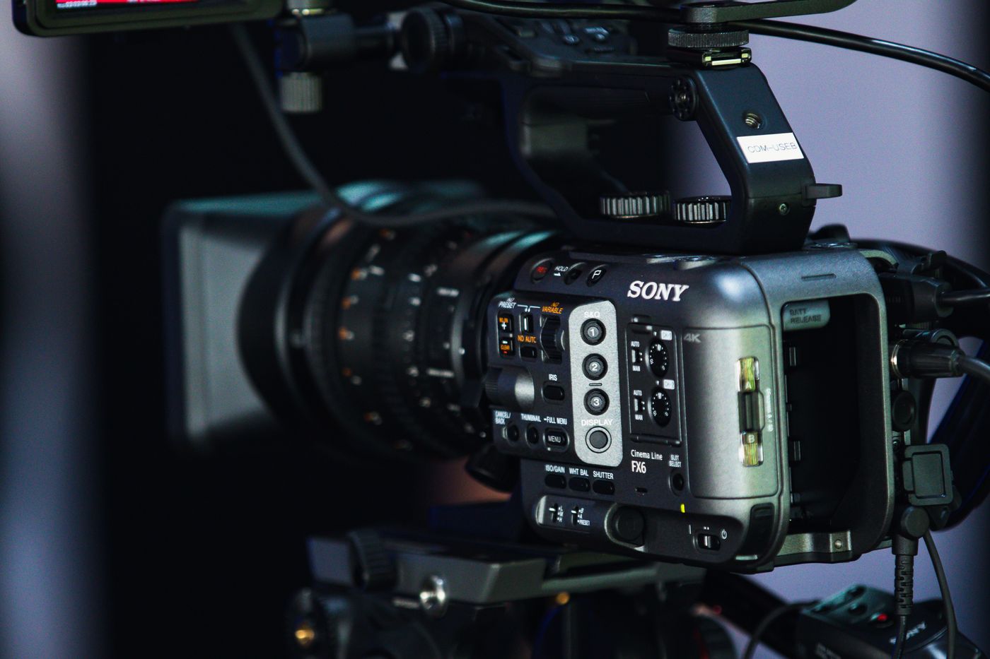 A cinema camera rigged on a tripod, picked out against a dark studio background.