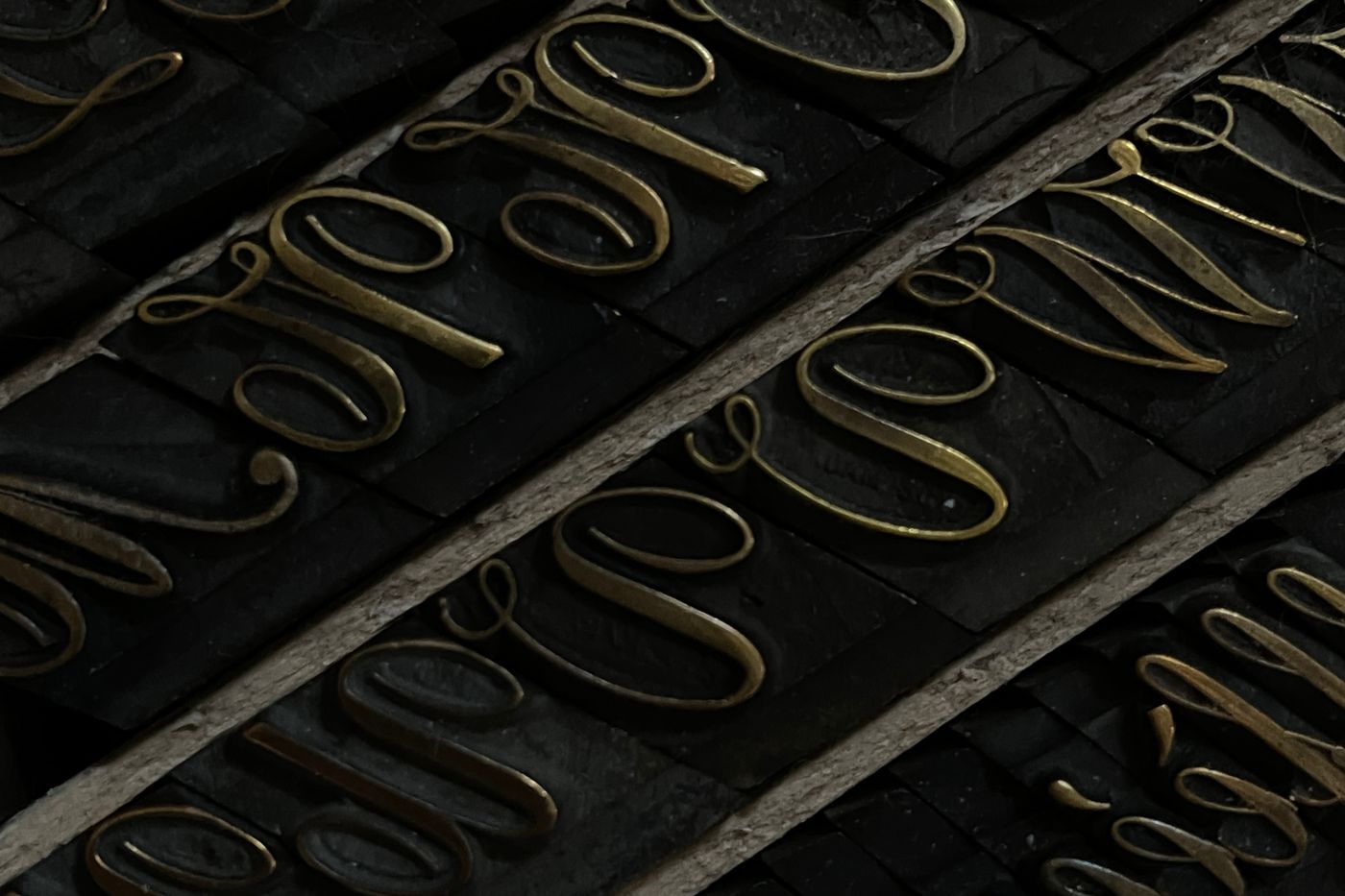 Rows of metal letterpress type in raking light, the letterforms catching the highlights.