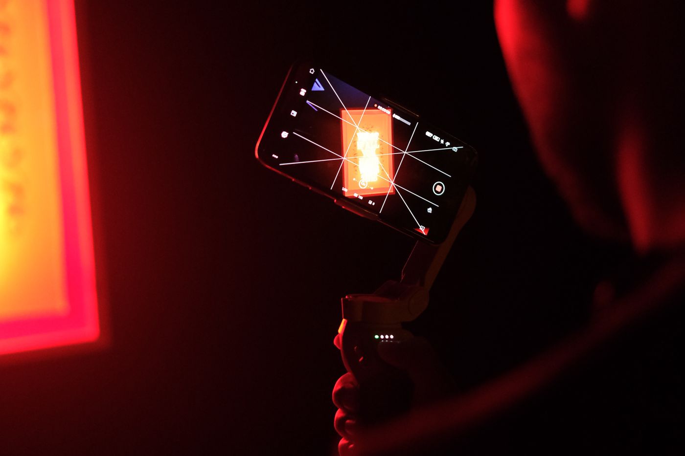 A smartphone mounted on a gimbal, recording vertical video against a red-lit wall.