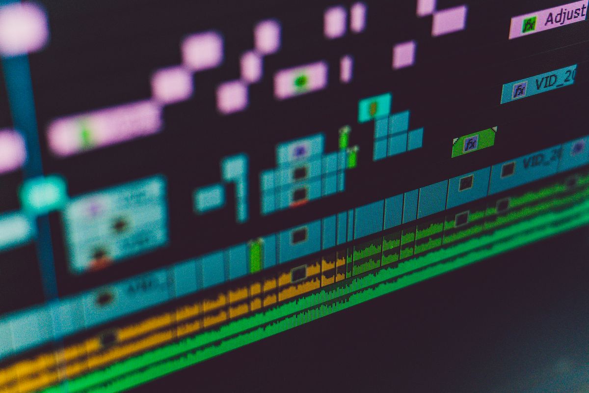 Angled close-up of a video-editing timeline, its clips stacked in green, pink and orange bands.