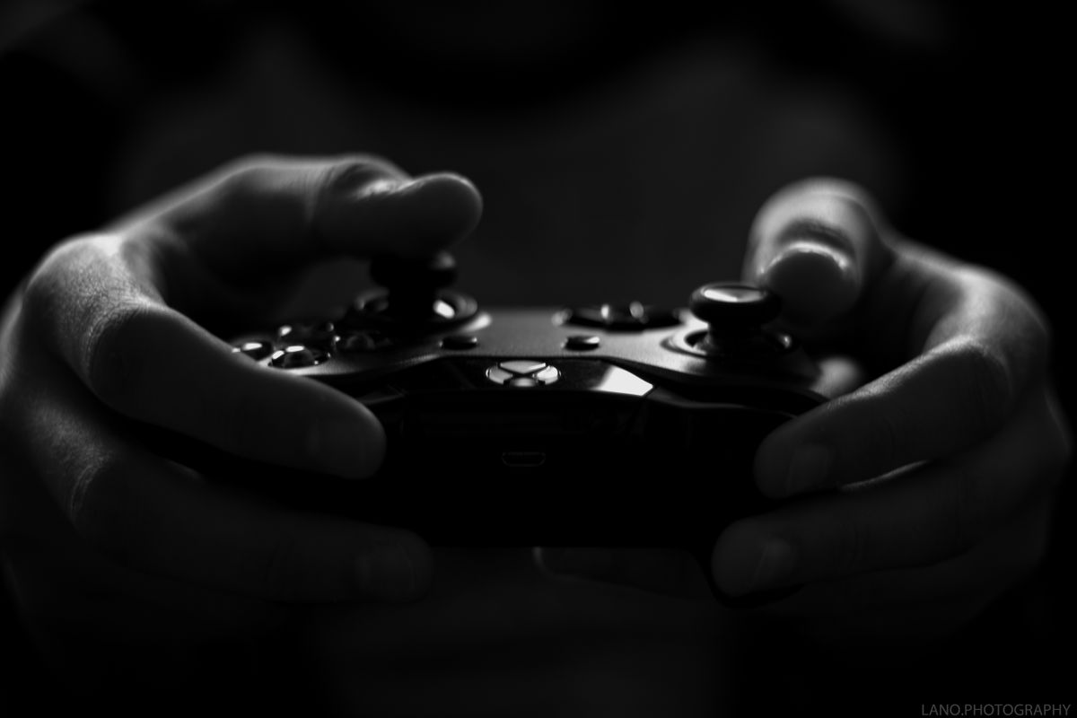 Two hands gripping a games controller, lit from one side against a black background.